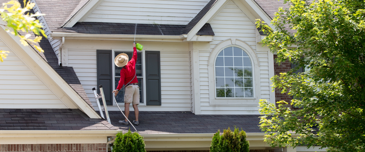 Man standing on roof cleaning black roof tiles.